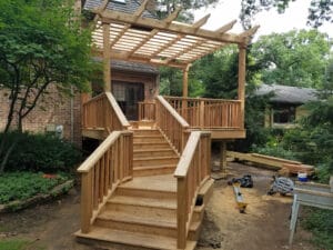 Front view of a staircase leading up to a newly built treated wood deck with a free-standing wood pergola.